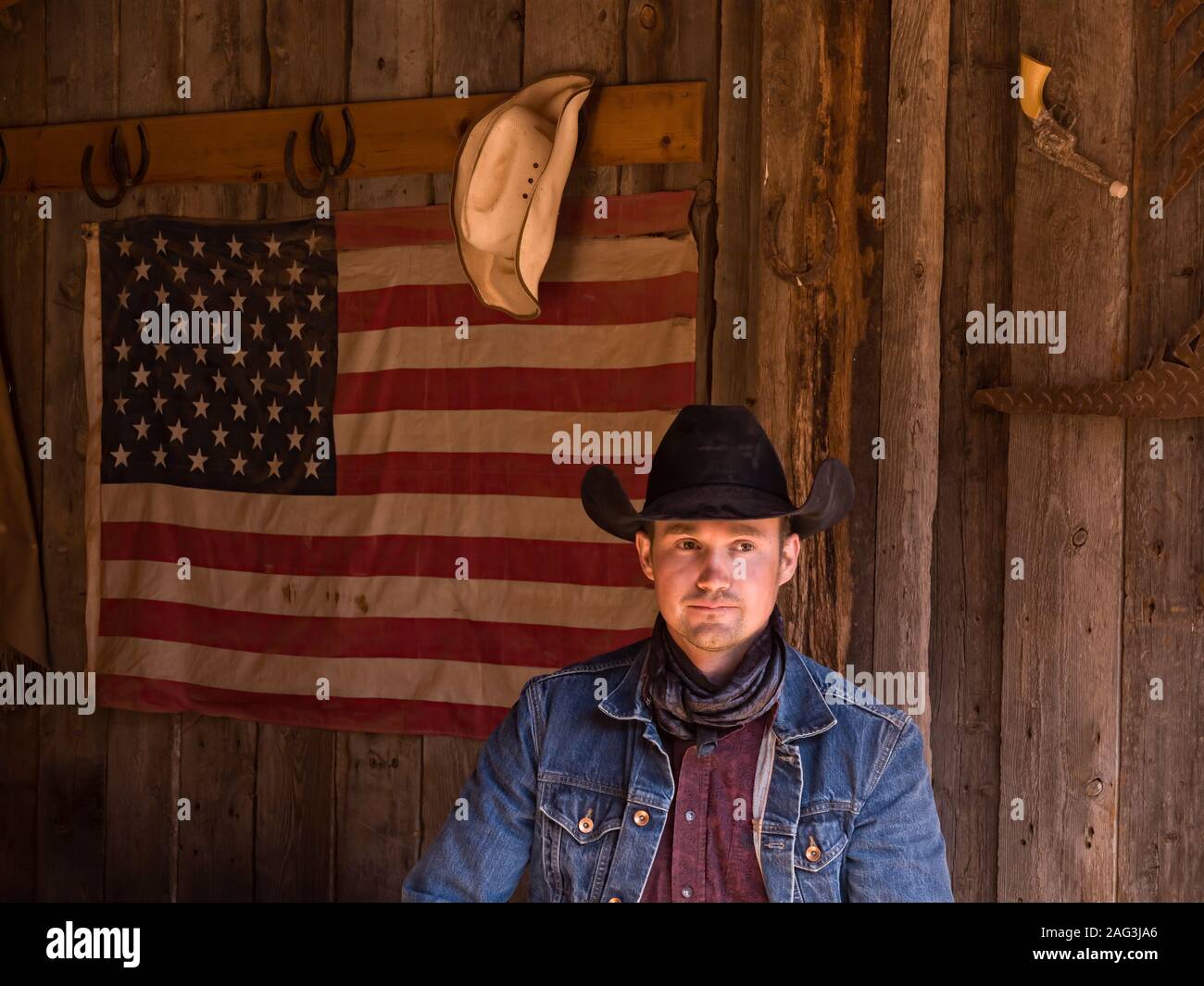 Un lavoro di cowboy wrangler pone nel suo cappello da cowboy e bandana  nella parte anteriore di una bandiera americana sulla Red cliffs ranch  vicino a Moab, Utah Foto stock - Alamy