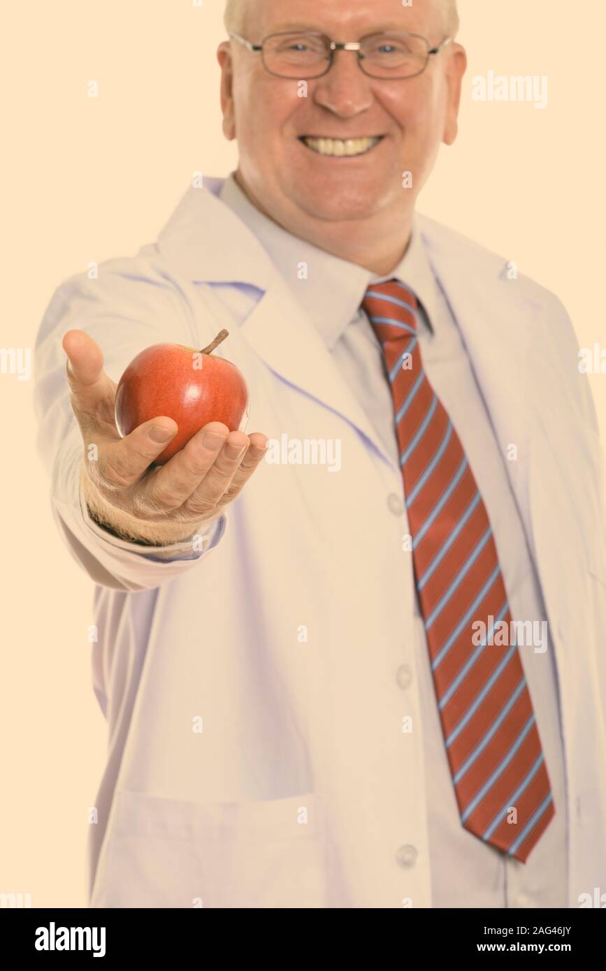 Studio shot di felice uomo maturo medico sorridere mentre dando red apple con focus su apple Foto Stock