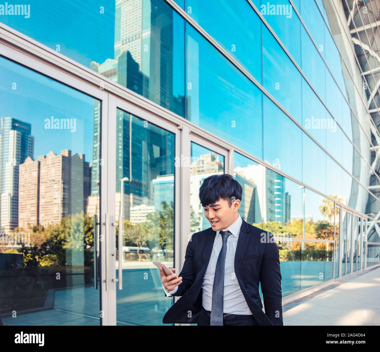 Uomo di business utilizzando il telefono cellulare e in piedi di fronte all edificio per uffici Foto Stock