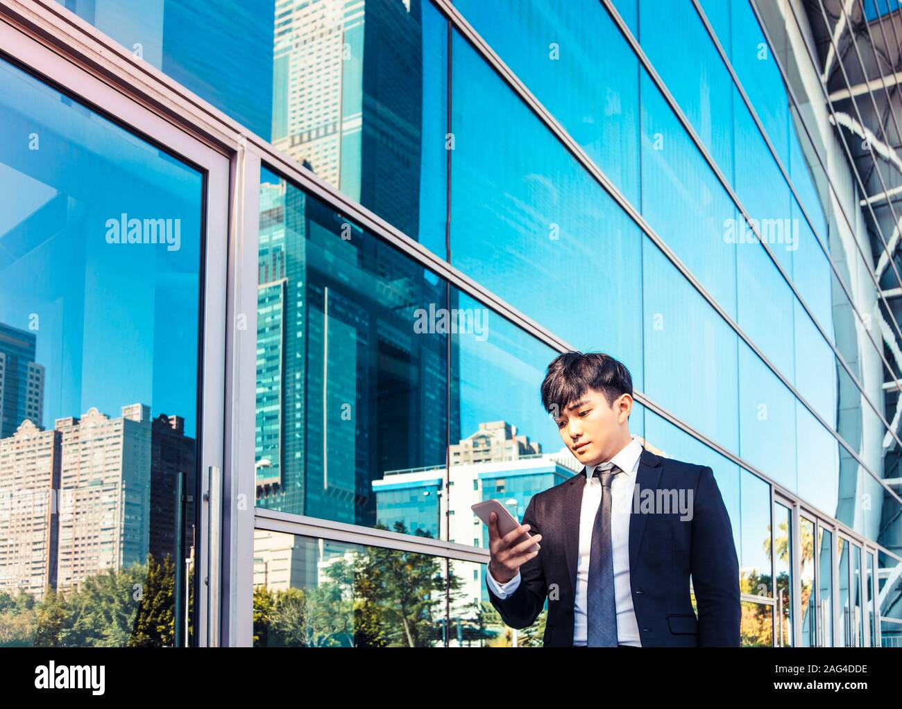Uomo di business utilizzando il telefono cellulare e in piedi di fronte all edificio per uffici Foto Stock