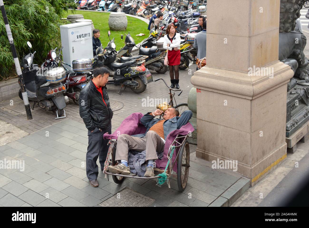 Shanghai, Cina - Novembre 08, 2014: uomo riposa in fatti in casa di risciò ciclo in corrispondenza di intersezione dove molti veicoli motorizzati sono parcheggiate. Foto Stock