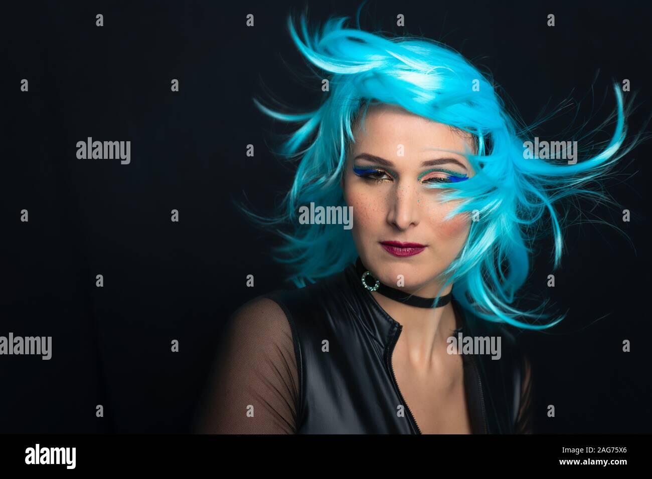 Una ragazza su uno sfondo nero con parrucca blu e i capelli al vento Foto Stock