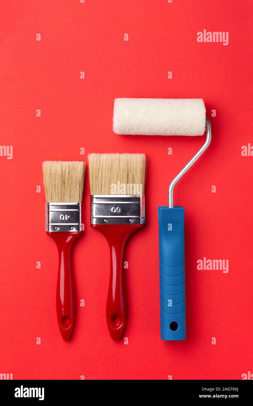 Rullo di vernice e due spazzole su sfondo rosso. Vista dall'alto in stile minimale il concetto di riparazione. Foto Stock