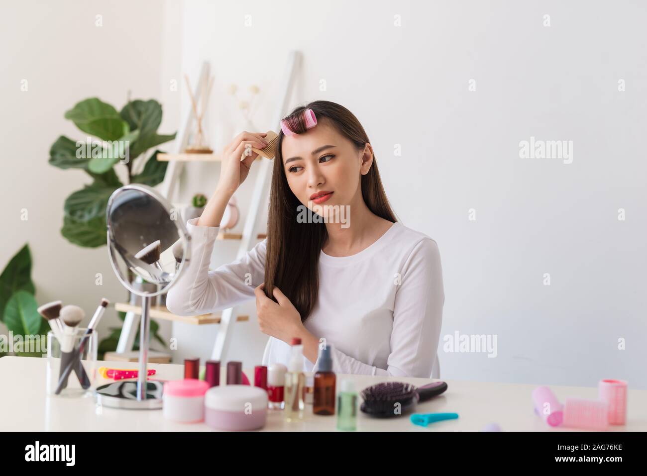 Tutorial di acconciatura. Donna asiatica spazzolare i capelli e sorridente piacevolmente durante le riprese di un tutorial per la sua bellezza blog Foto Stock