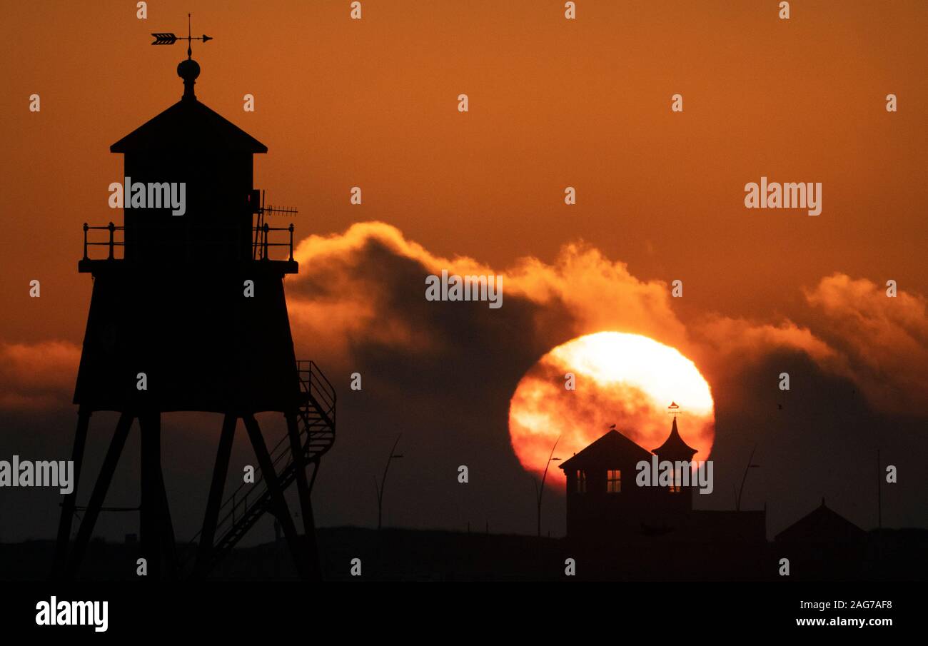 Il sole sorge oltre la mandria Groyne faro a South Shields sulla costa nord est. Foto Stock