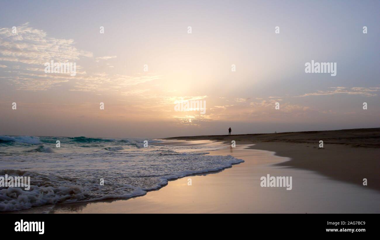 Una persona che gode di una passeggiata serale in una appartata spiaggia tropicale in Capo Verde al tramonto Foto Stock