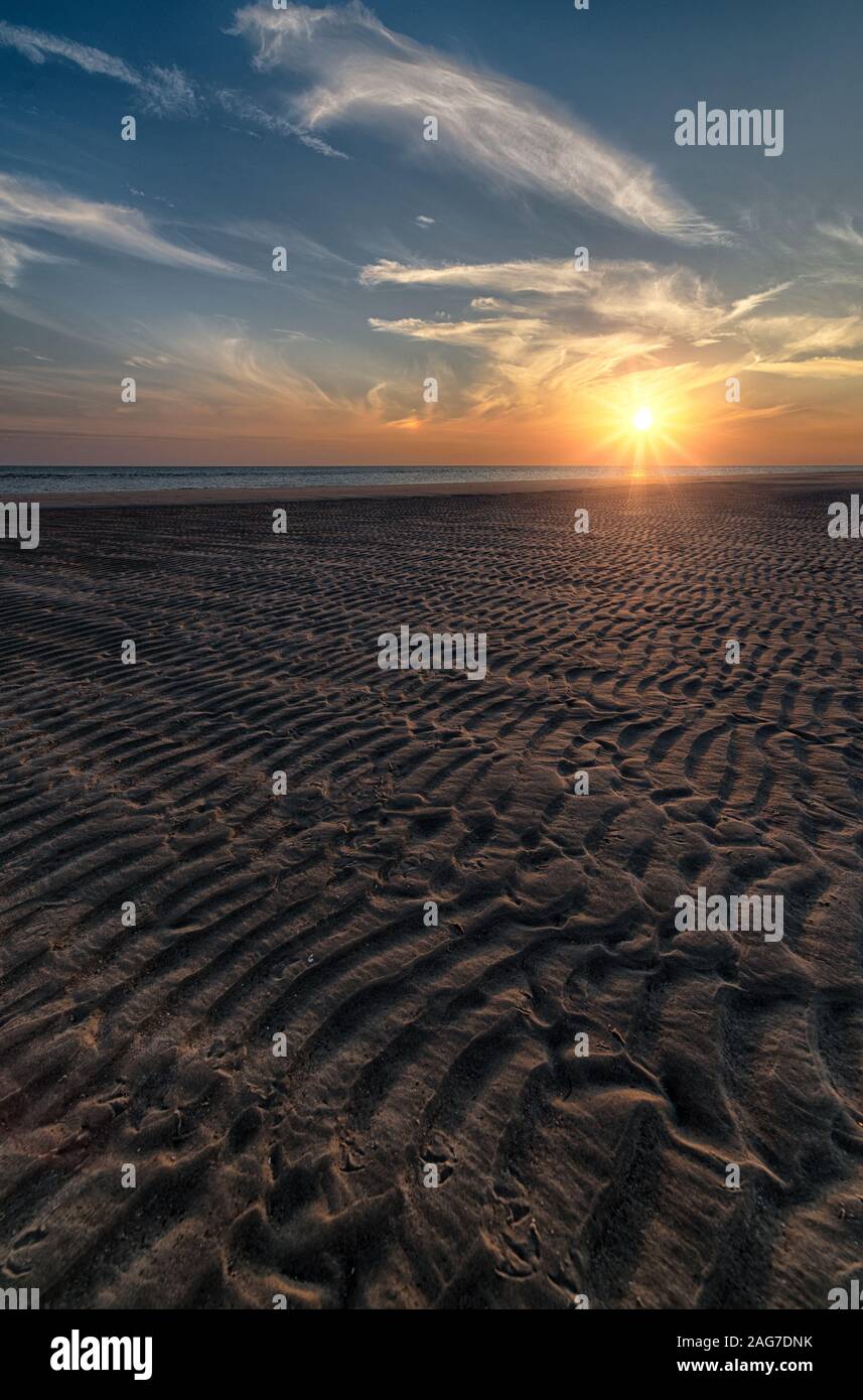 Scatto verticale di una bella alba sulla spiaggia che crea il paesaggio perfetto per le passeggiate mattutine Foto Stock