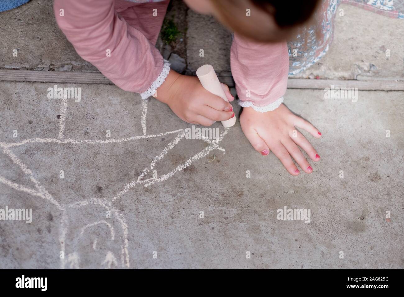 Le mani di una ragazza di disegno con gesso bianco su un percorso concreto Foto Stock Le mani di una ragazza di disegno con gesso bianco su un percorso concreto Foto Stock