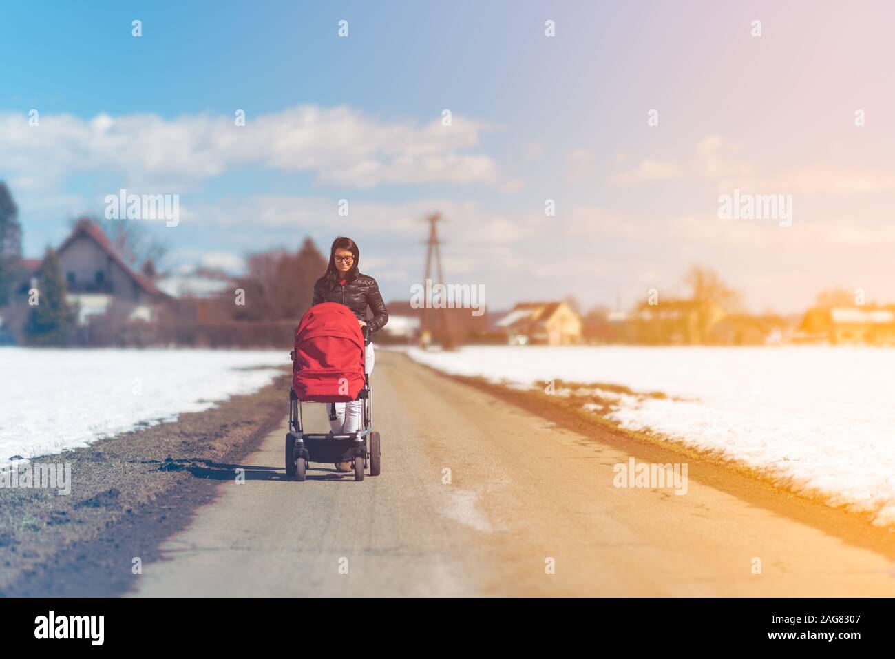 Il bambino nel passeggino rosso i campi in campagna con la madre. Relax nella natura in inverno giornata di sole. Foto Stock