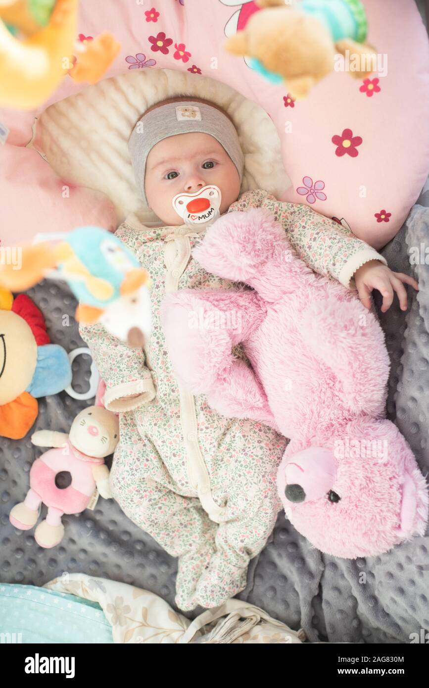 Happy Baby girl giacente nel suo presepe con succhietto e orso rosa Foto Stock