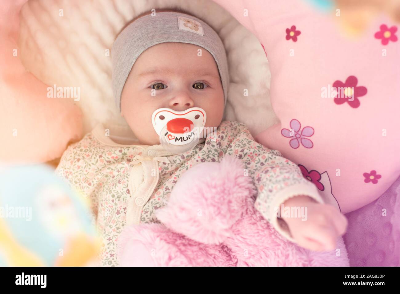 Happy Baby girl giacente nel suo presepe con succhietto e orso rosa Foto Stock