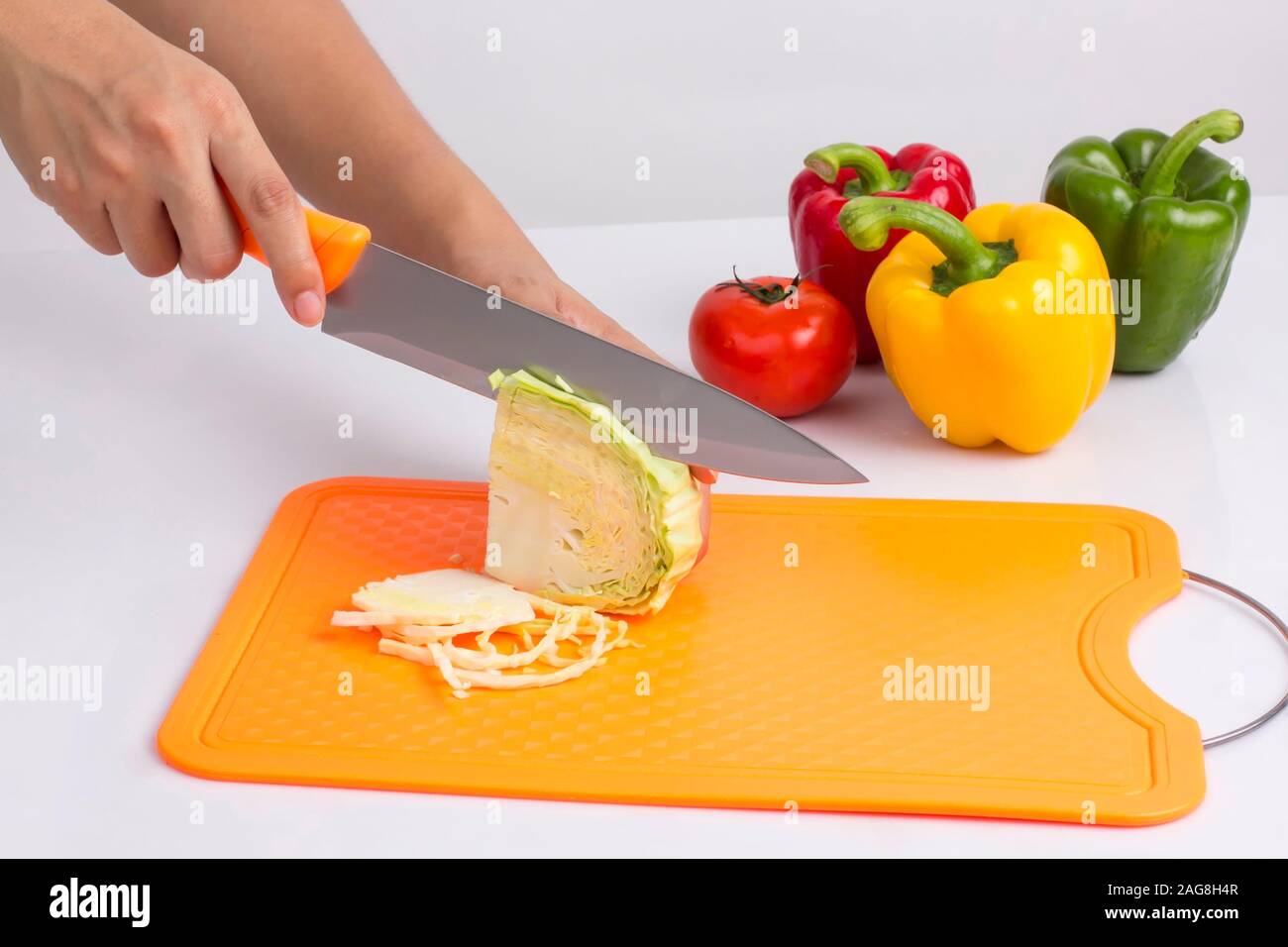 Casalinga cavolo di taglio con il coltello sulla plastica tagliere su sfondo bianco Foto Stock