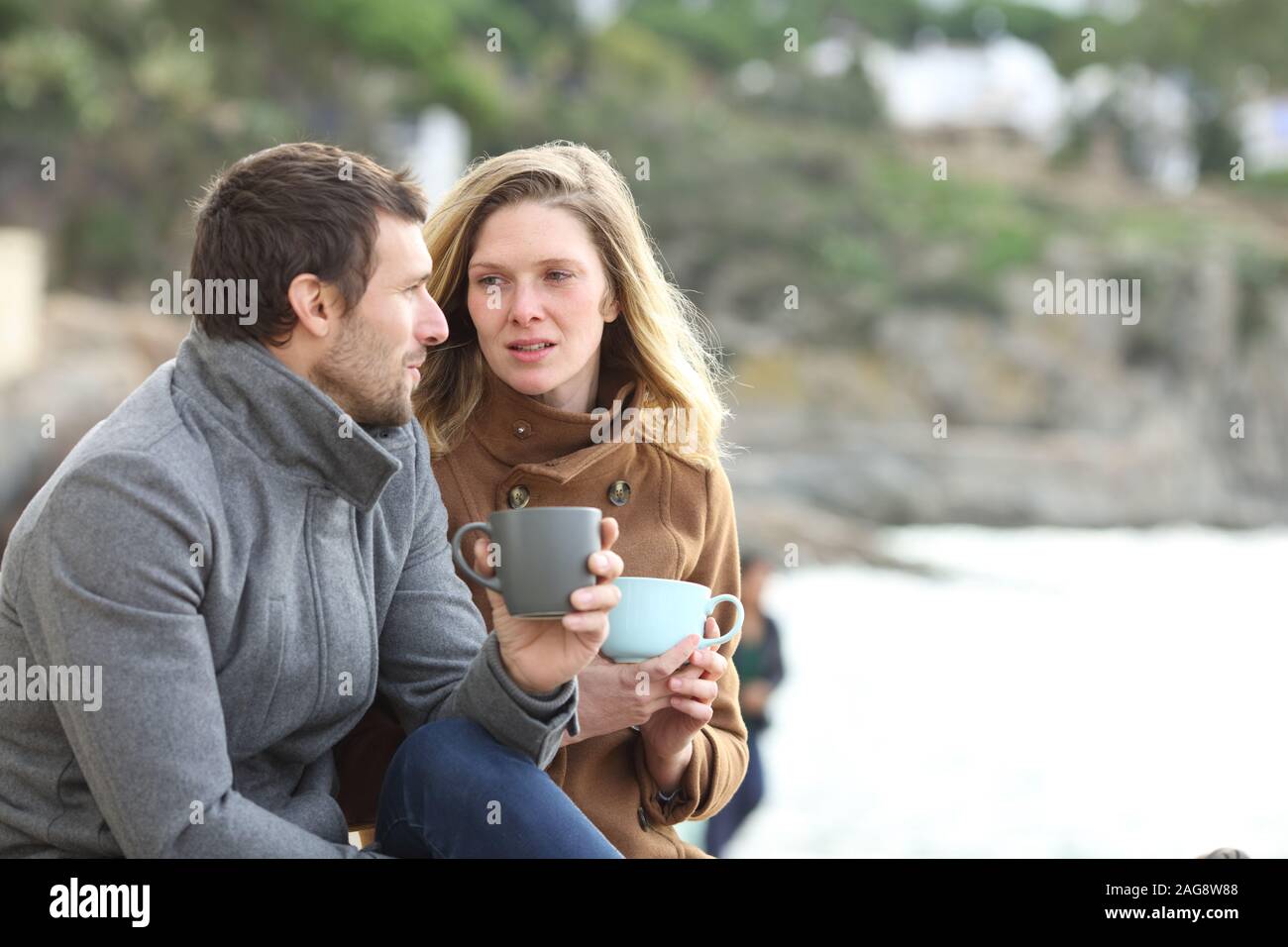 Grave giovane di adulti di parlare seduto e di bere il caffè in inverno sulla spiaggia Foto Stock