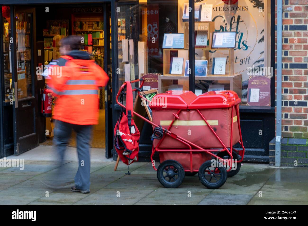 Un postino o postwoman consegna la posta utilizzando un carrello o su carrello, la persona post è sfocata per mostrare il movimento Foto Stock