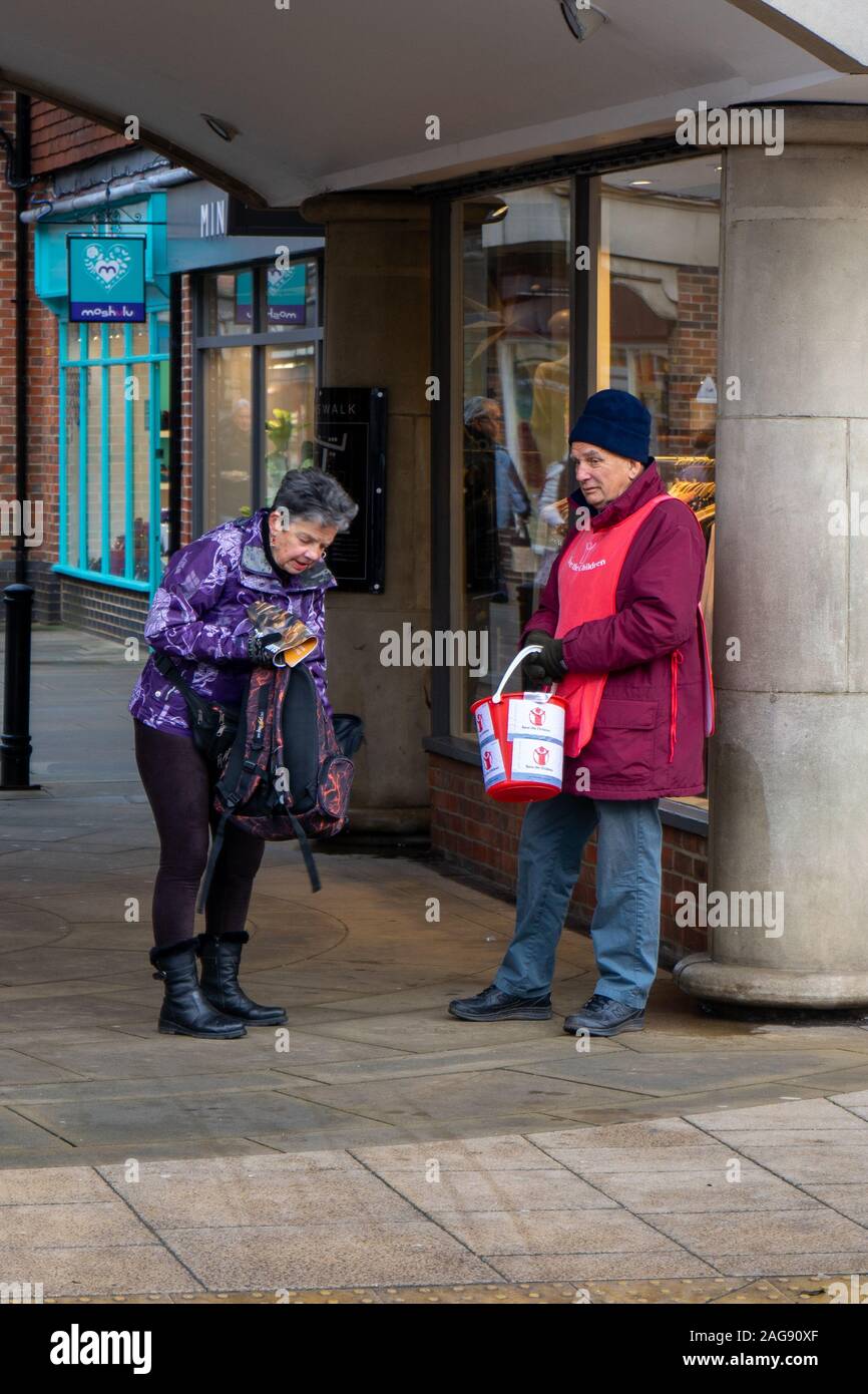 Una donna di mezza età ottenere le monete dal suo portafoglio per dare ad un collettore di carità in strada Foto Stock