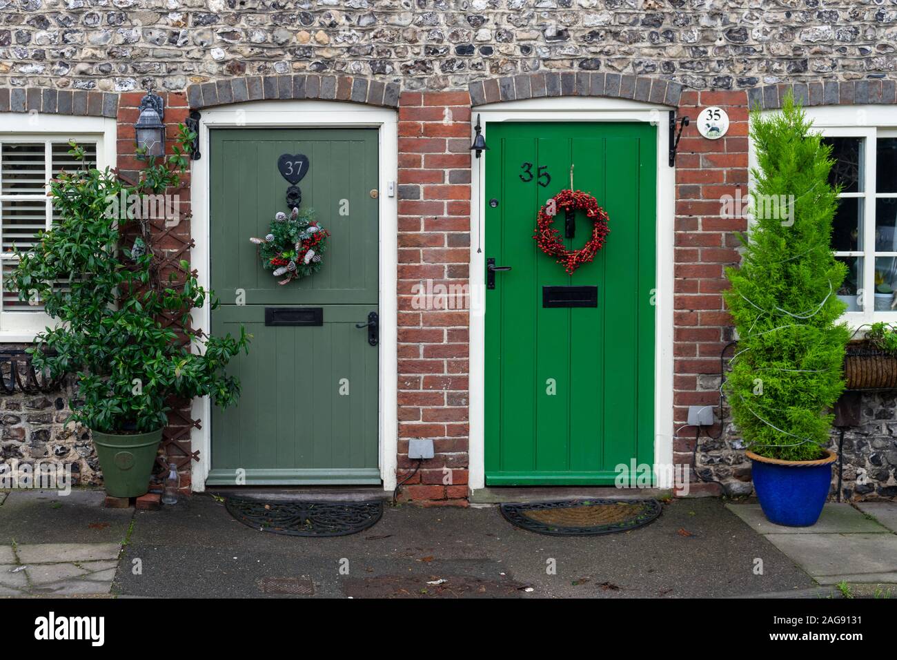 Natale ghirlande appeso al legno Porte anteriori su due mattoni inglese cottage Foto Stock
