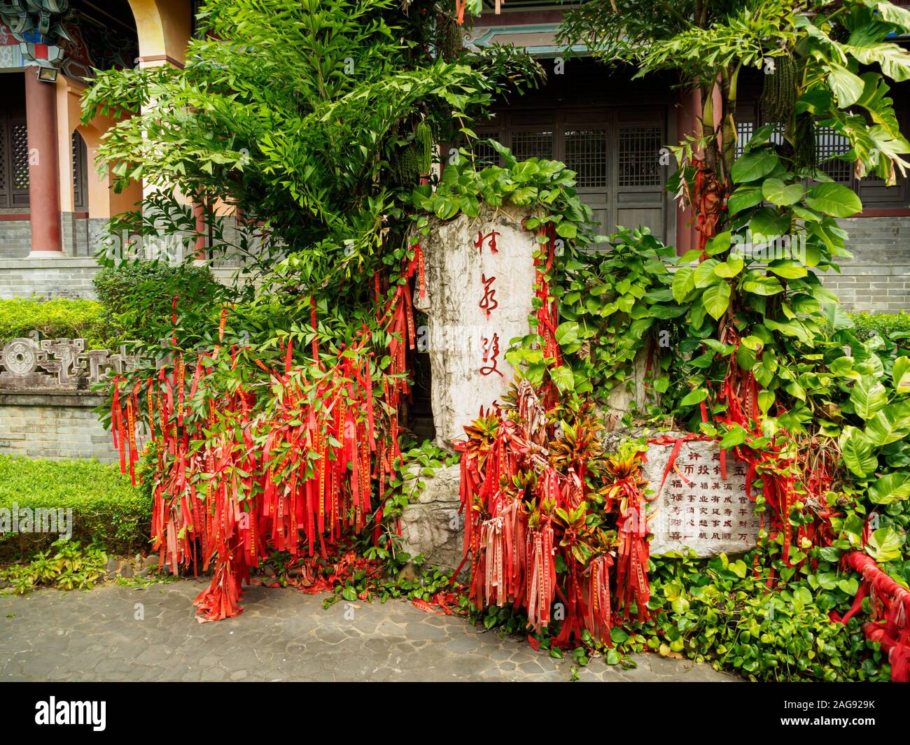 Nastri di colore rosso su una wishing tree in un tempio cinese di Hainan in Cina. Credo cinese che lasciando un nastro rosso appeso su un wishing tree renderà thei Foto Stock