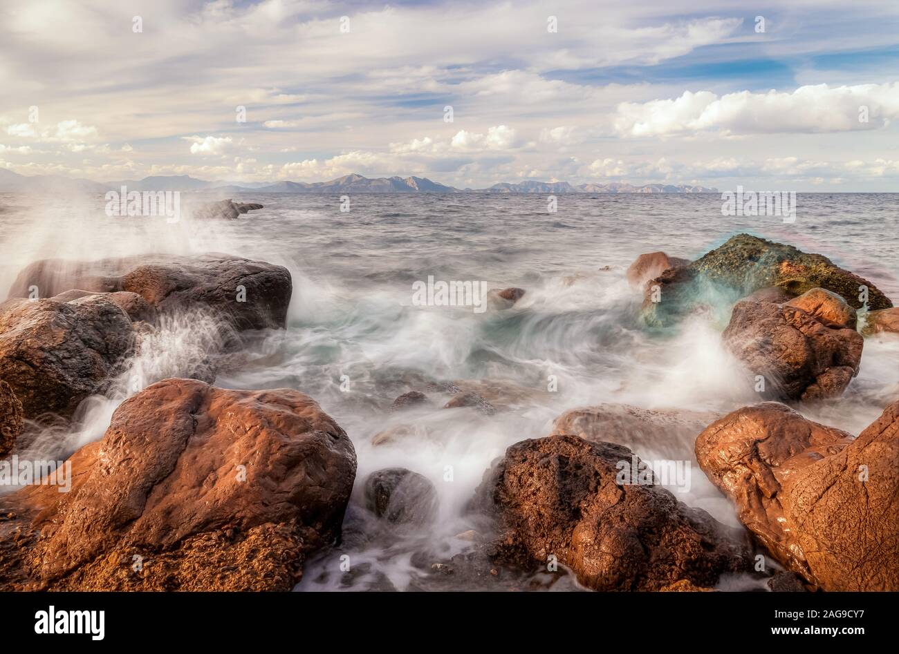 Mare Mediterraneo si infrangono sulle rocce a Platja des Calo nei pressi di Betlem e Colonia de Sant Pere con Cap de Formentor sullo sfondo azzurro del cielo e wh Foto Stock