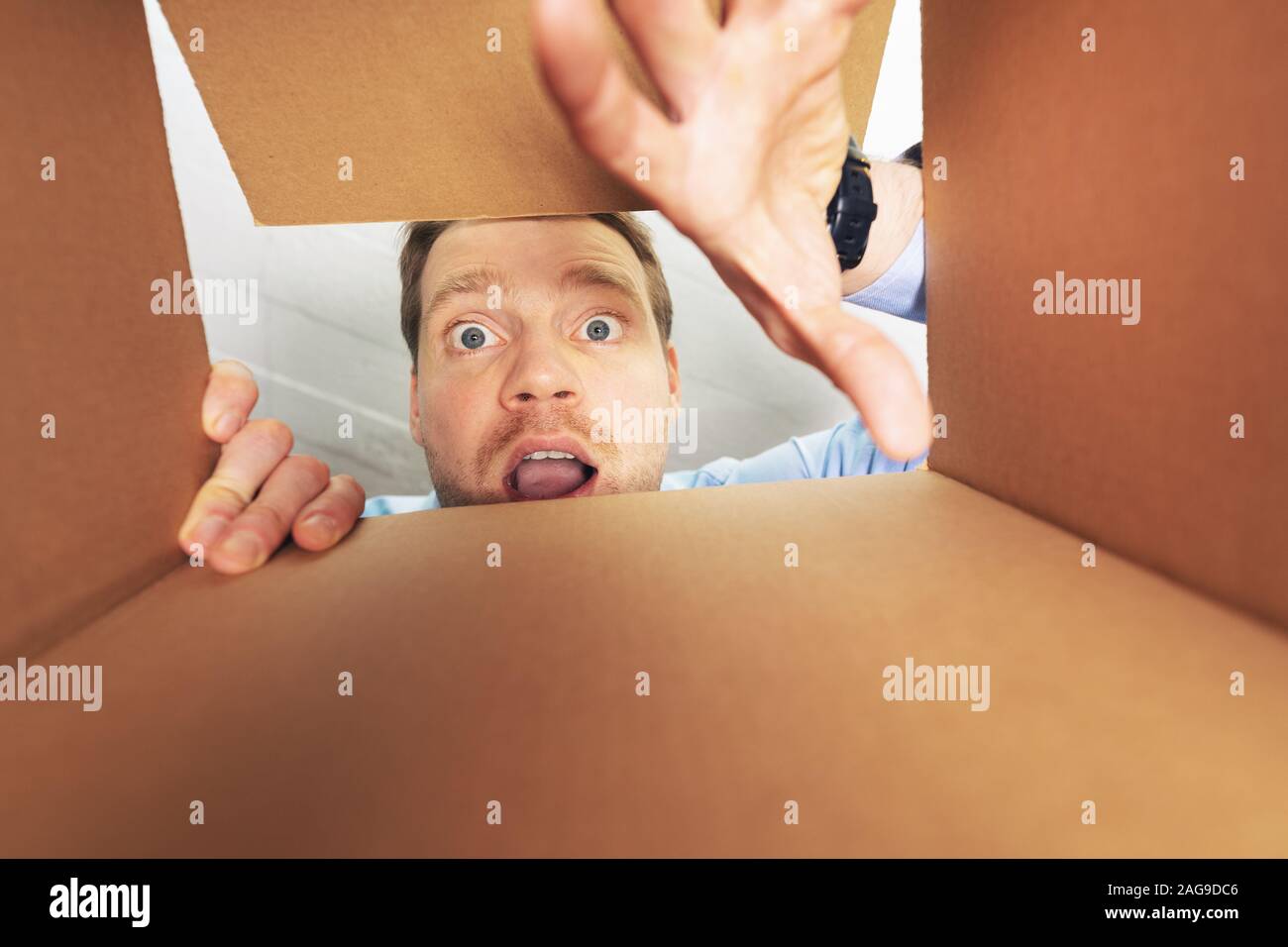 Uomo eccitato per aprire la scatola di cartone e guardando all'interno Foto Stock