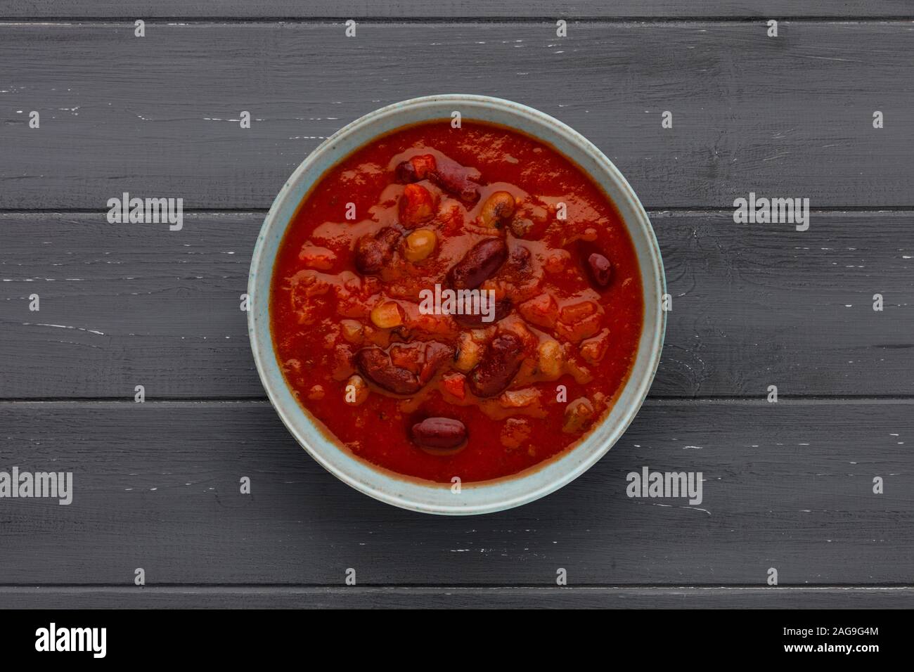 Una tazza di delizioso peperoncino minestra di fagioli in una ciotola rustico, su un invecchiato in legno scuro di sfondo, con spazio per la copia. Foto Stock