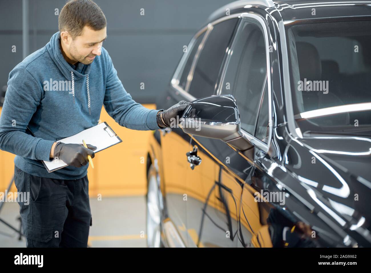 Auto di servizio lavoratore esaminando il corpo del veicolo per i graffi e i danni, prendendo un auto per auto professionali dettagliati. Professional body auto il concetto di ispezione Foto Stock