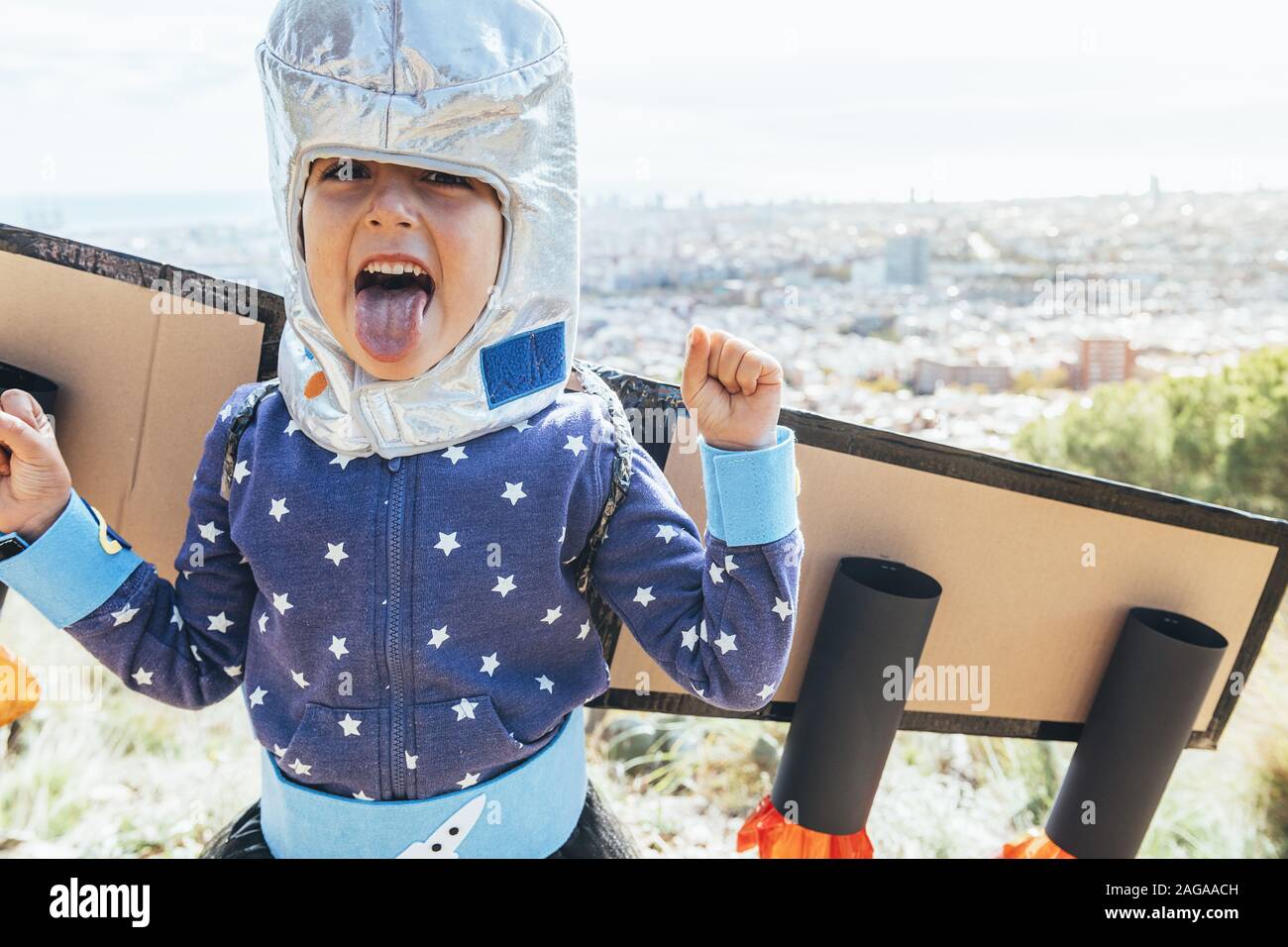 Ritratto di un divertente bambino ragazza sporgenti dalla sua lingua dissimulata come un supereroe con costumi fatti in casa, cartone piano ali e astronauta timone Foto Stock
