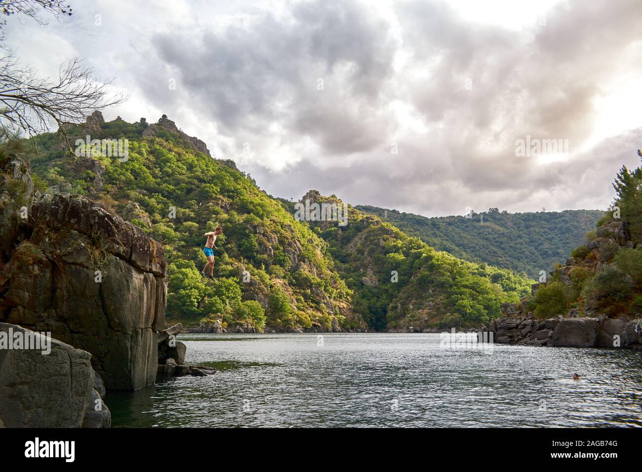Giovane uomo di saltare su l'acqua su un lago nella foresta giorno nuvoloso Foto Stock