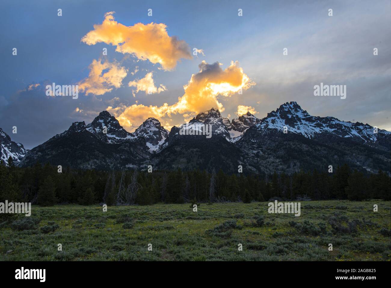 Nuvole colorate da un tramonto arancione dietro i pepici della catena montuosa del Grand Teton con luce drammatica e ombre profonde contrastanti Foto Stock