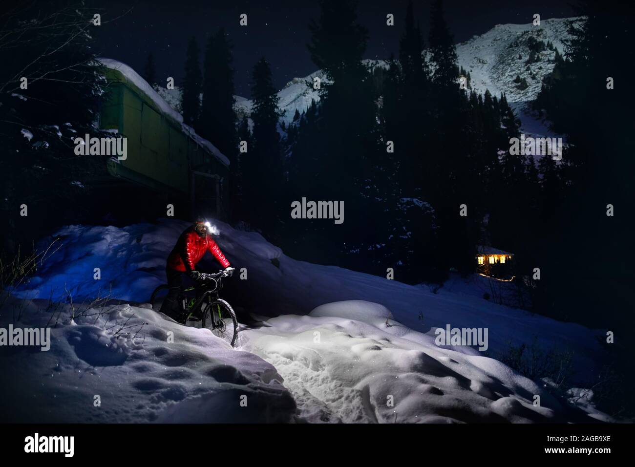 Uomo in camicia rossa con la bicicletta a inverno boschi innevati in montagna sotto il cielo notturno con stelle Foto Stock