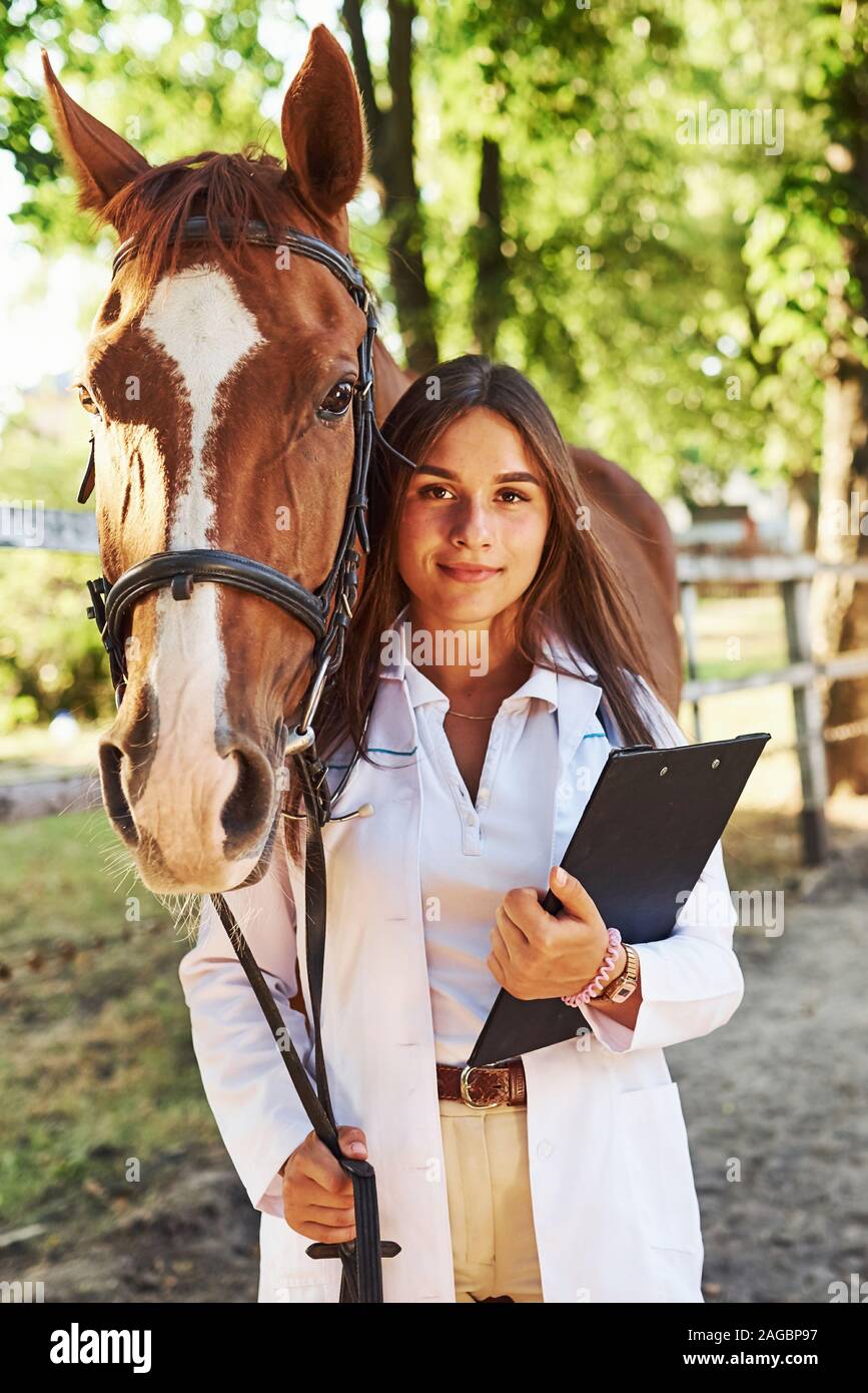 Con il blocco note in mani. Femmina esaminando vet horse all'aperto presso la fattoria di giorno Foto Stock