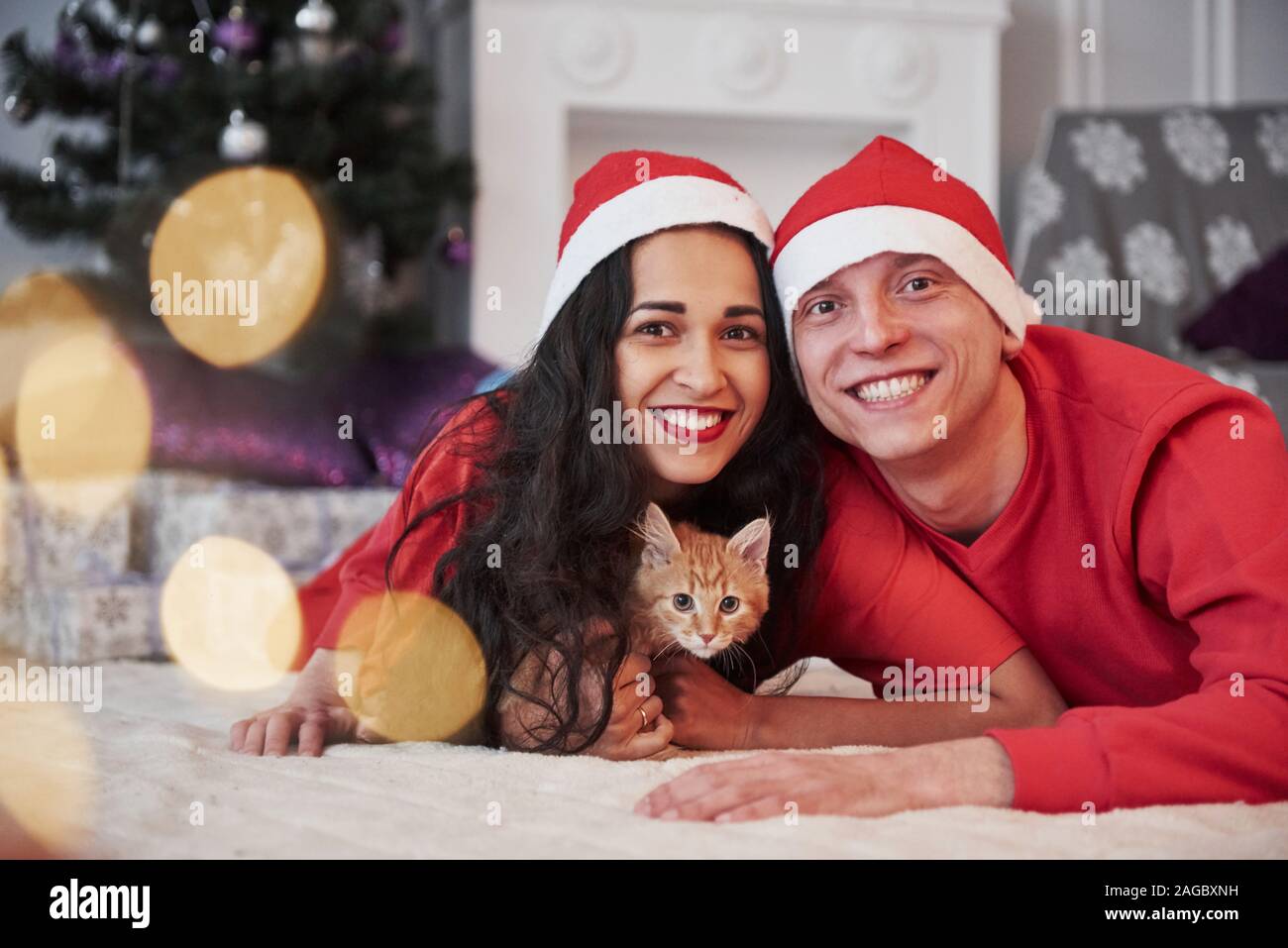 Sdraiato sul pavimento. Tutti comprese cat guardando nella telecamera. Ritratto di giovane con poco kitty celebra vacanze nel nuovo anno vestiti Foto Stock