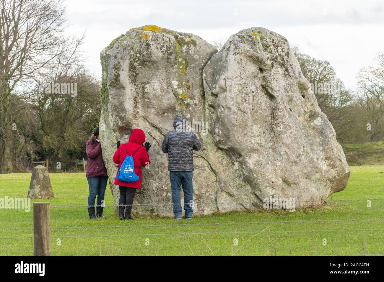 I visitatori ad Avebury Stone Circle toccando e abbracciando il neolitihic pietre per l'energia magnetica e di poteri di guarigione, Wiltshire, Inghilterra, Regno Unito Foto Stock