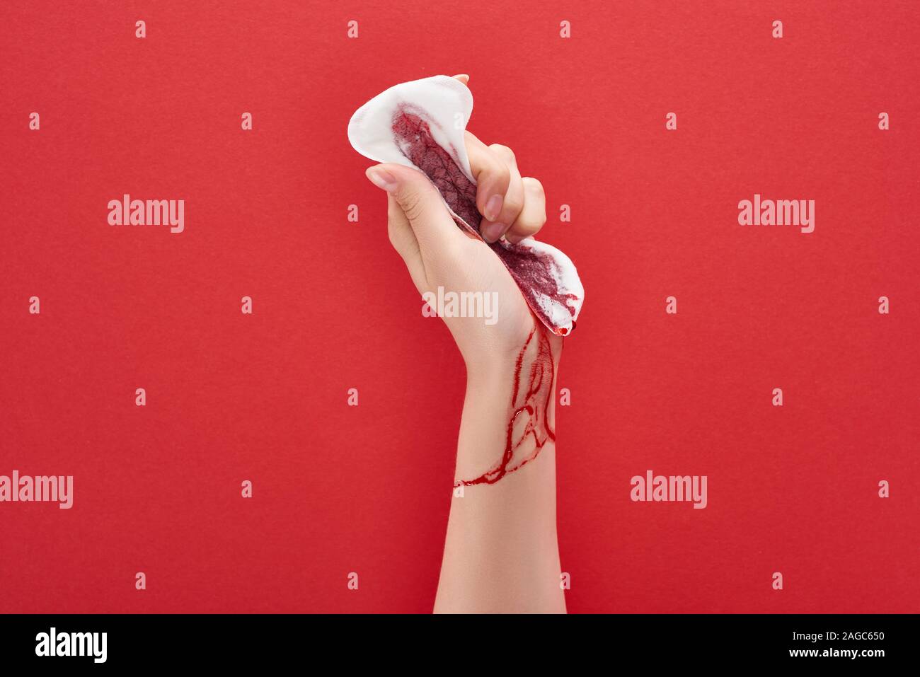 Vista parziale della donna la spremitura di assorbente igienico con il sangue su sfondo rosso Foto Stock