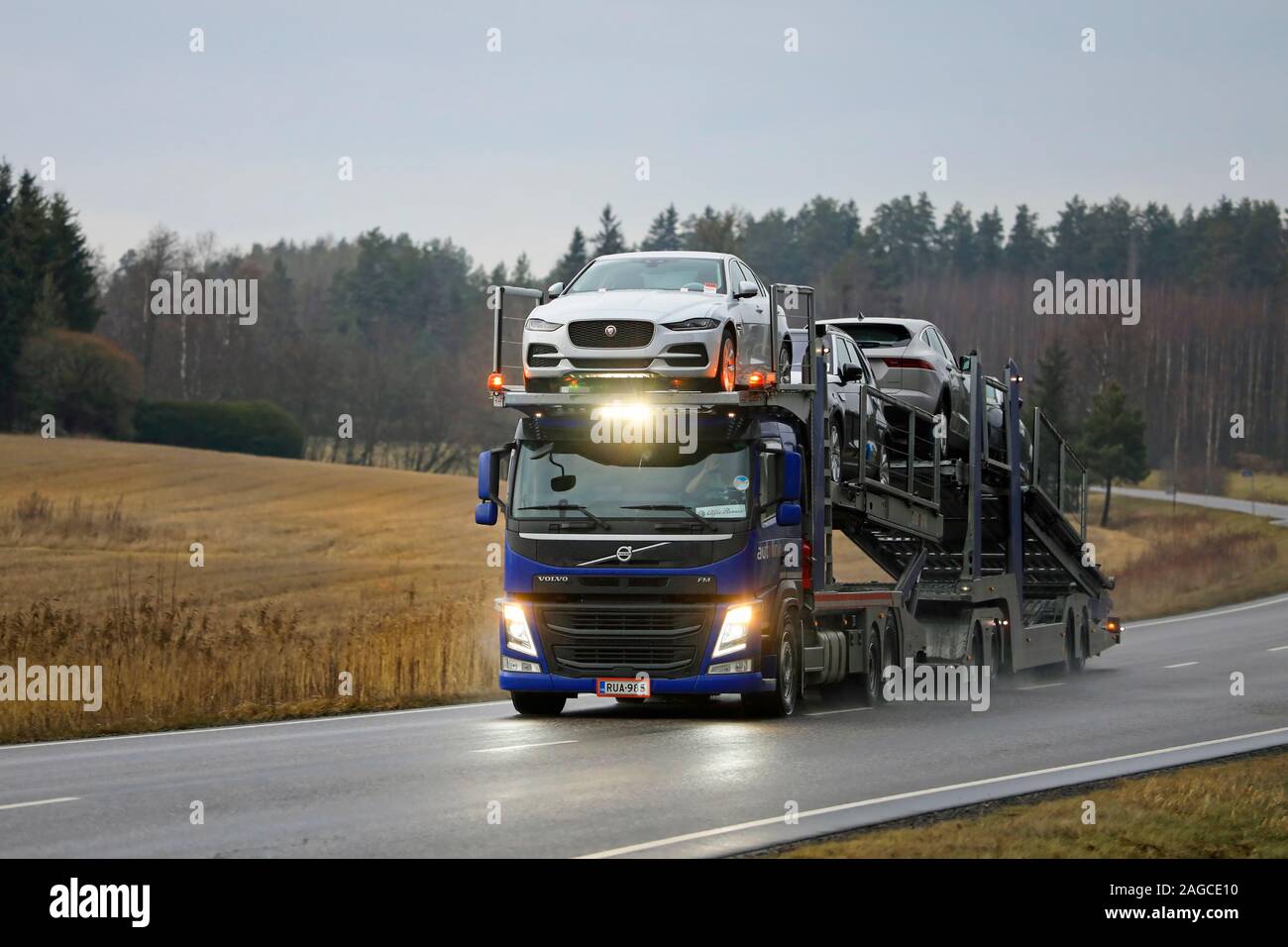 Blue VOLVO FM auto vettore Autolink carrello con carico di nuove automobili Jaguar si accende dark autostrada in un pomeriggio d'inverno. Salo, Finlandia. Dicembre 13, 2019. Foto Stock