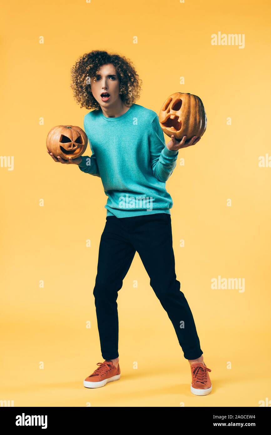 Spaventata curly adolescente holding zucche di Halloween su giallo Foto Stock