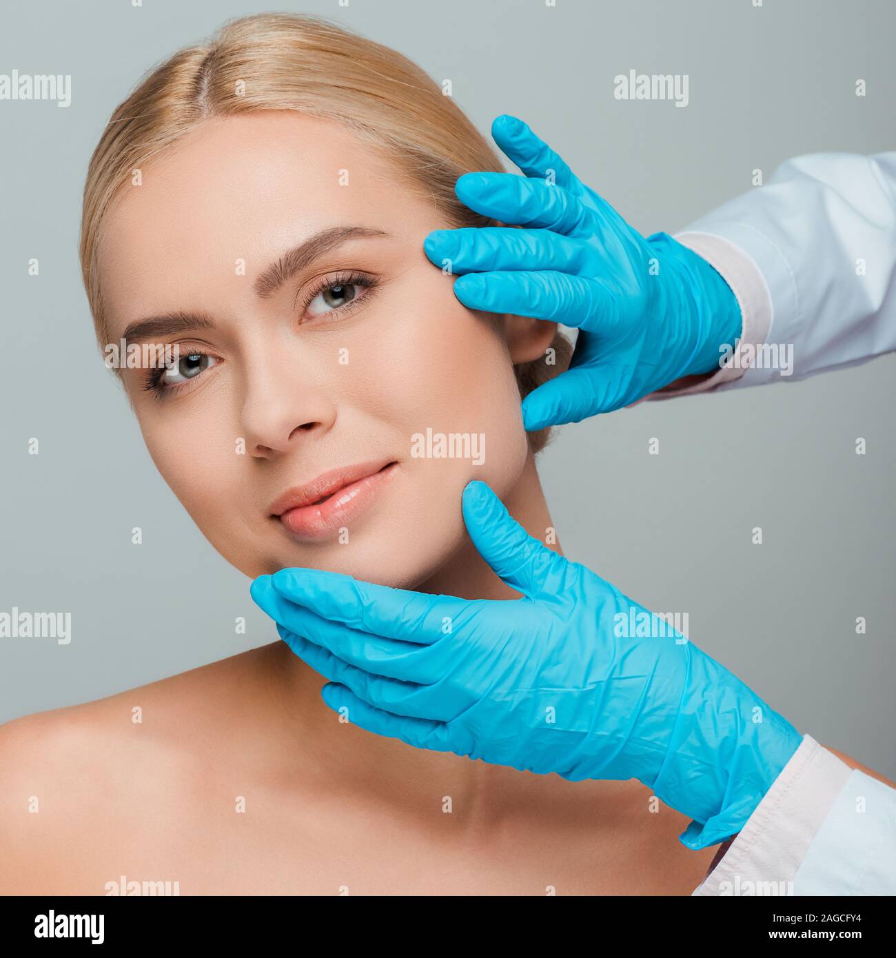 Vista ritagliata di estetista in guanti in lattice toccando volto di  giovane donna isolato su grigio Foto stock - Alamy