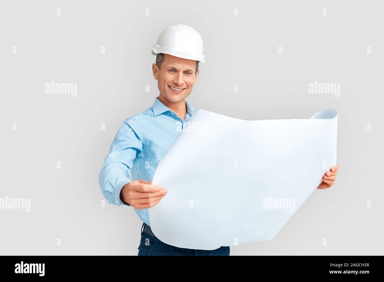 Costruzione. Uomo maturo in hardhat in piedi isolato su bianco con blueprint sorridendo felice Foto Stock