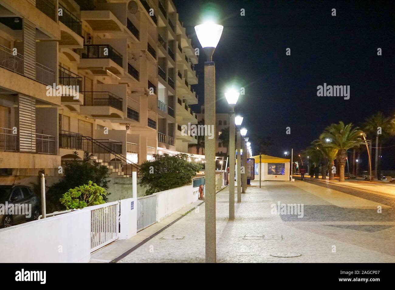 Quarteira, passeggiata del Portogallo di notte, con appartamenti sulla sinistra e palme e la spiaggia sulla destra. Foto Stock