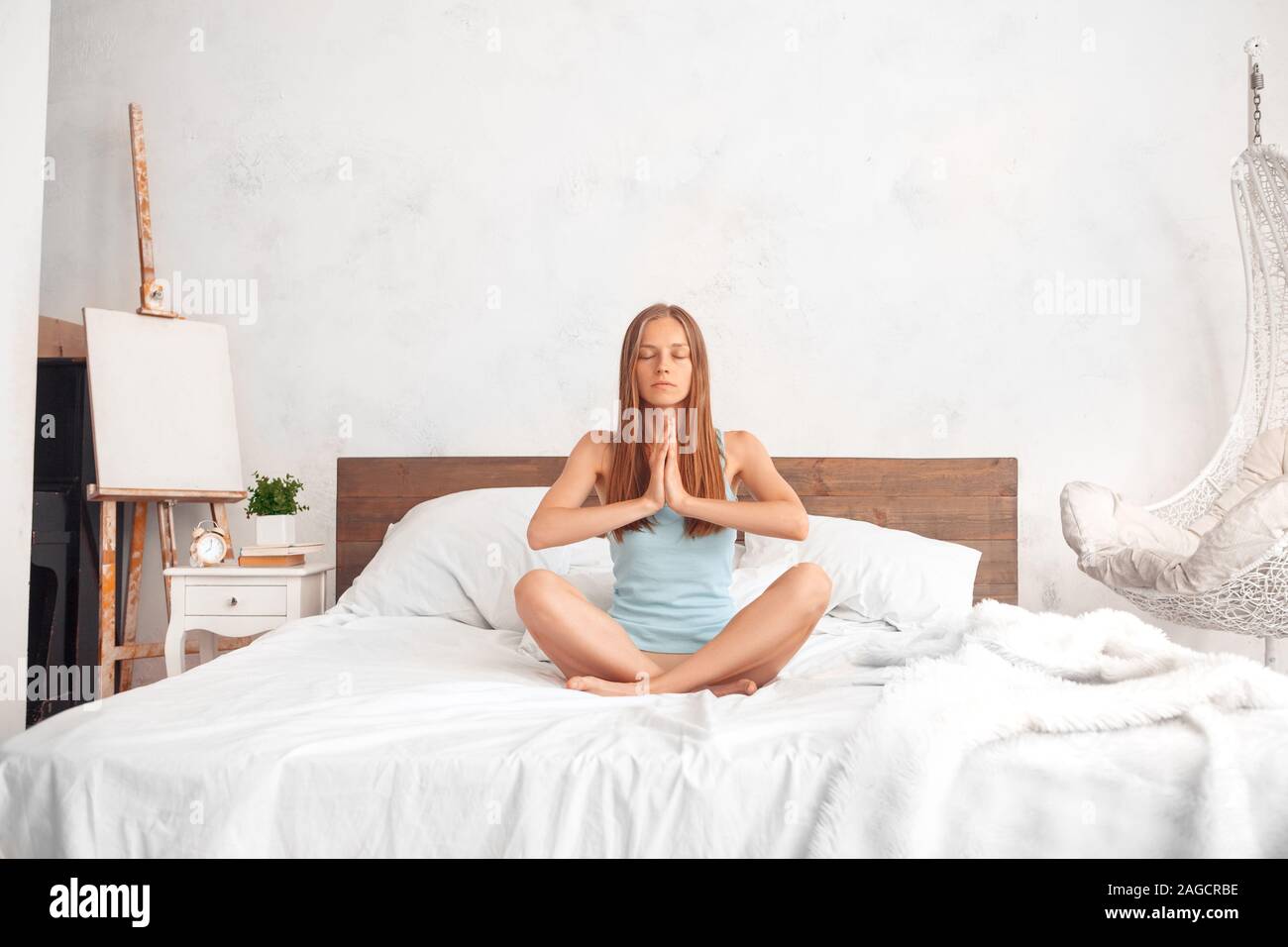Mattinata a casa. Donna seduta in lotus pongono sul letto mano nella preghiera meditando tranquillo Foto Stock