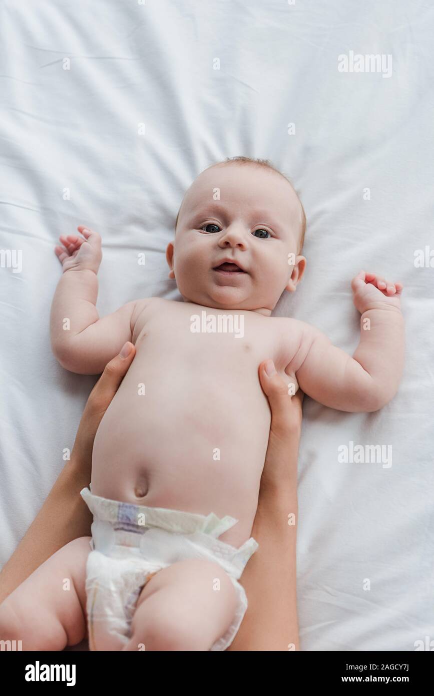 Vista superiore della madre tenendo in armi simpatico baby figlia guardando la fotocamera Foto Stock