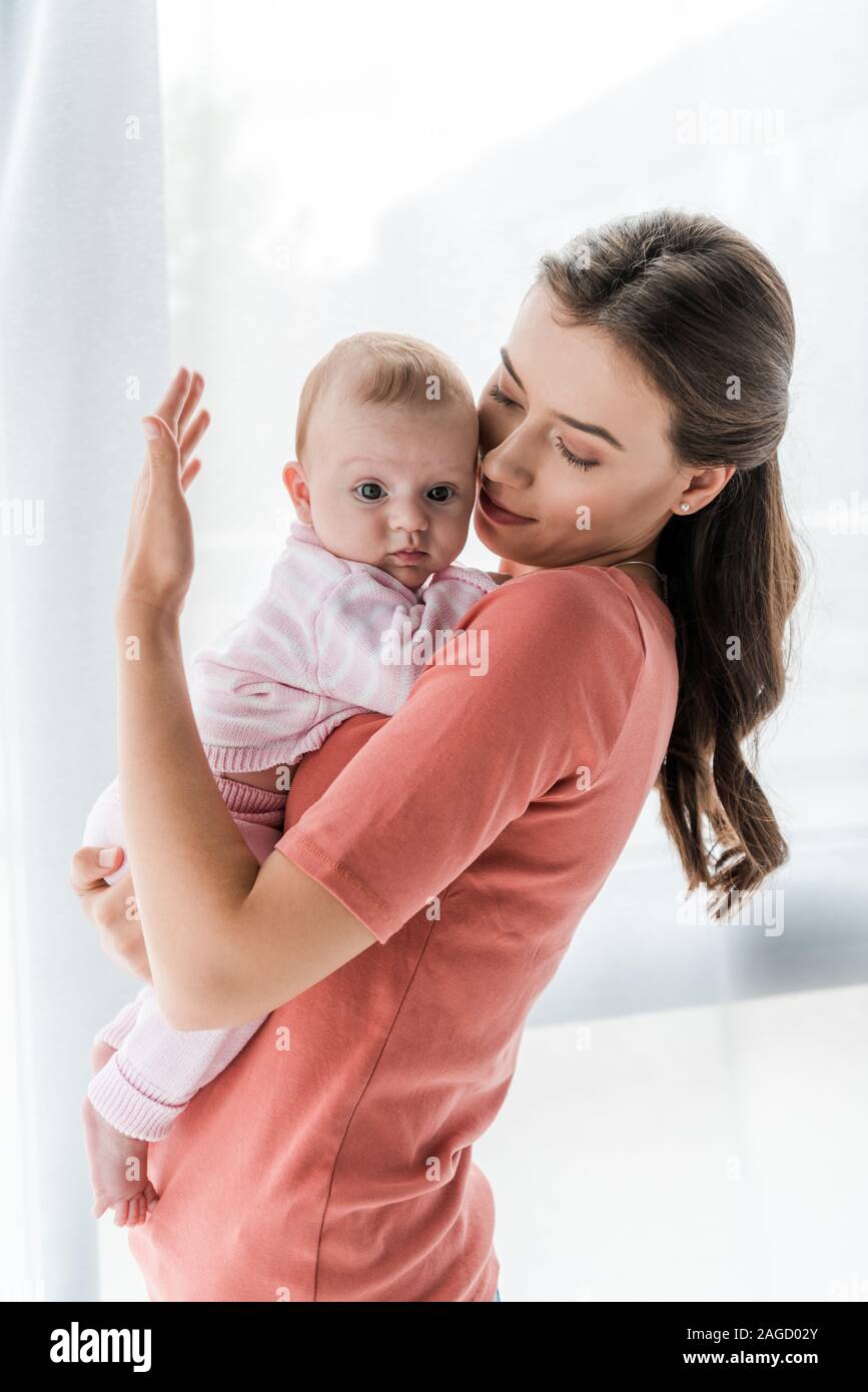 Attraente madre tenendo in armi bimba a casa Foto Stock