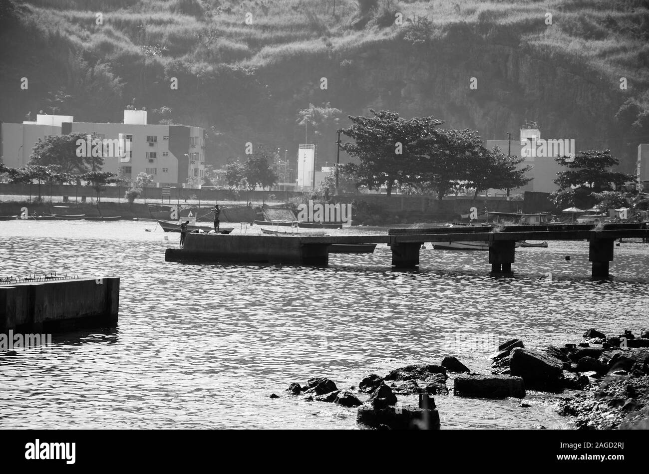 Immagine in scala di grigi del mare con le navi, un ponte e la gente circondata da colline e verde Foto Stock
