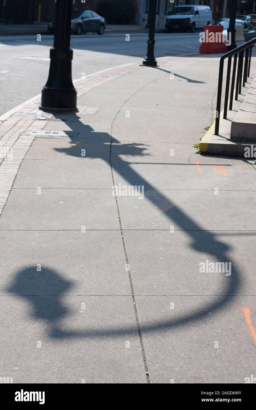 La lunga ombra di un lampione su un marciapiede urbano nel tardo pomeriggio. Foto Stock