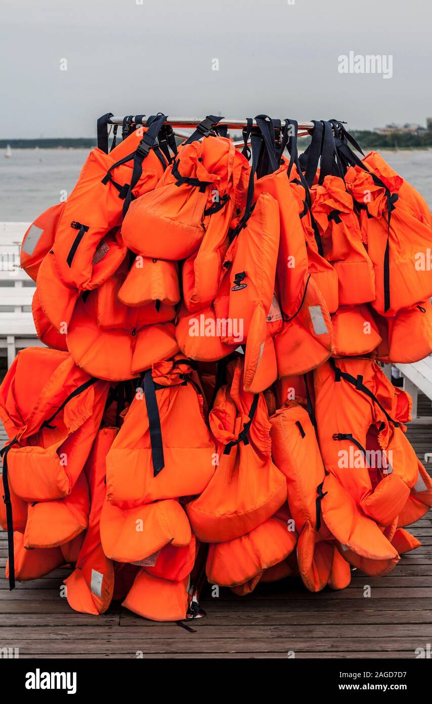 Molti orange giubbotti di salvataggio appesa sulla cremagliera sul molo del mare Foto Stock