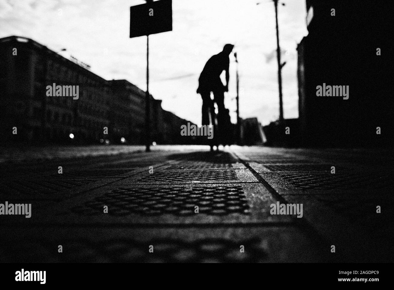 Foto in scala di grigi ad angolo basso di una persona che guida una bicicletta sulla strada Foto Stock