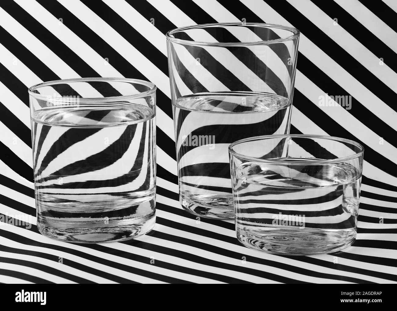 Superficie a strisce bianche e nere con tre bicchieri riempiti con acqua - ottimo per uno sfondo Foto Stock