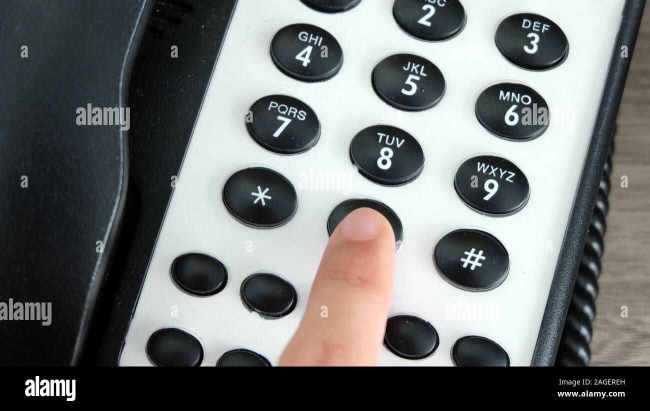 Mano premendo il tasto 0 tasto di composizione di un telefono di ufficio. Foto Stock