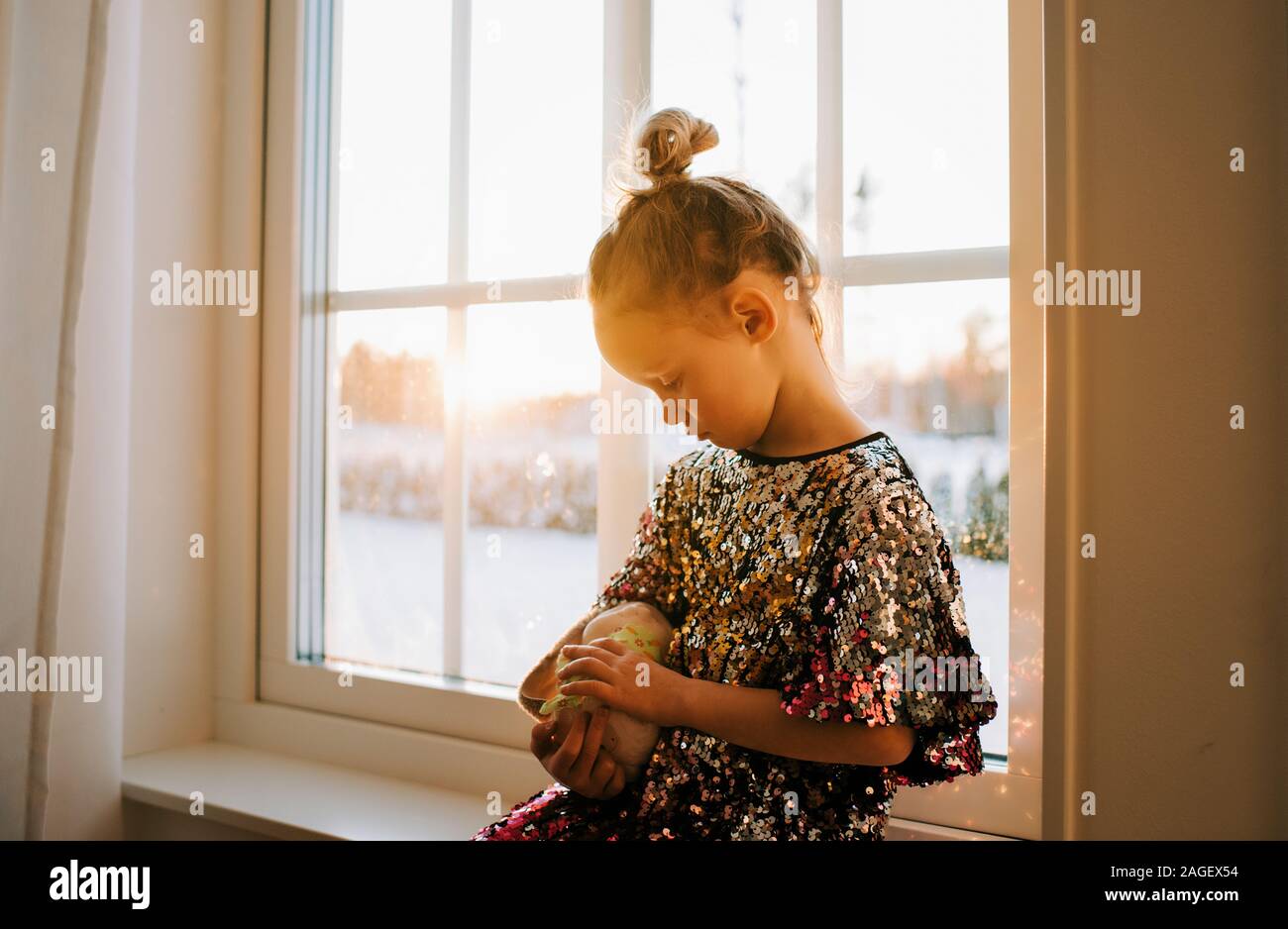 Ragazza giovane cuddling il suo giocattolo in un abito di scintillanti a casa al tramonto Foto Stock