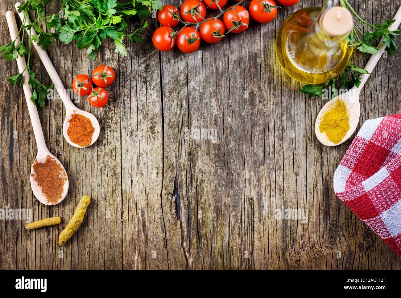 Vista superiore dei vari ingredienti alimentari su vintage tavolo in legno. Mix di spezie, cherry pomodoro, erbe aromatiche e olio di oliva su sfondo rustico da sopra. Per la cottura Foto Stock