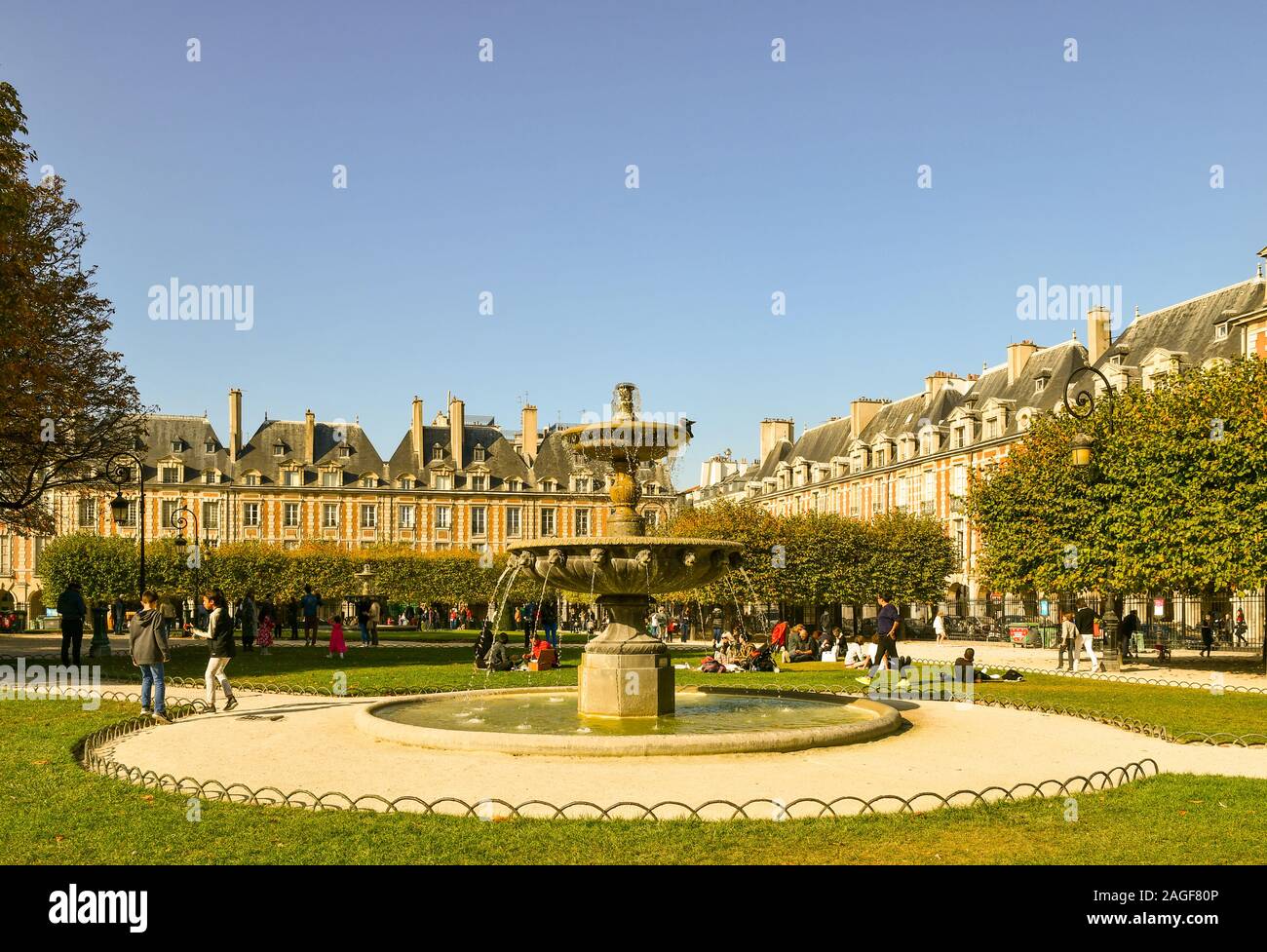 Vista di Place des Vosges, la famosa piazza nel quartiere di Marais, con una fontana di pietra e persone rilassante in una soleggiata giornata autunnale, Parigi, Francia Foto Stock